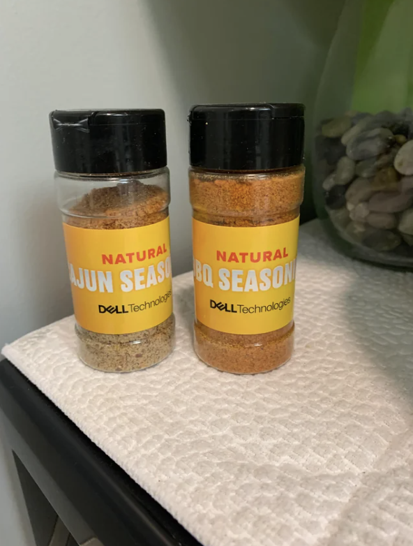 Two spice bottles labeled "Natural Cajun Season" and "Natural BBQ Season" by DELL Technologies, on a white surface