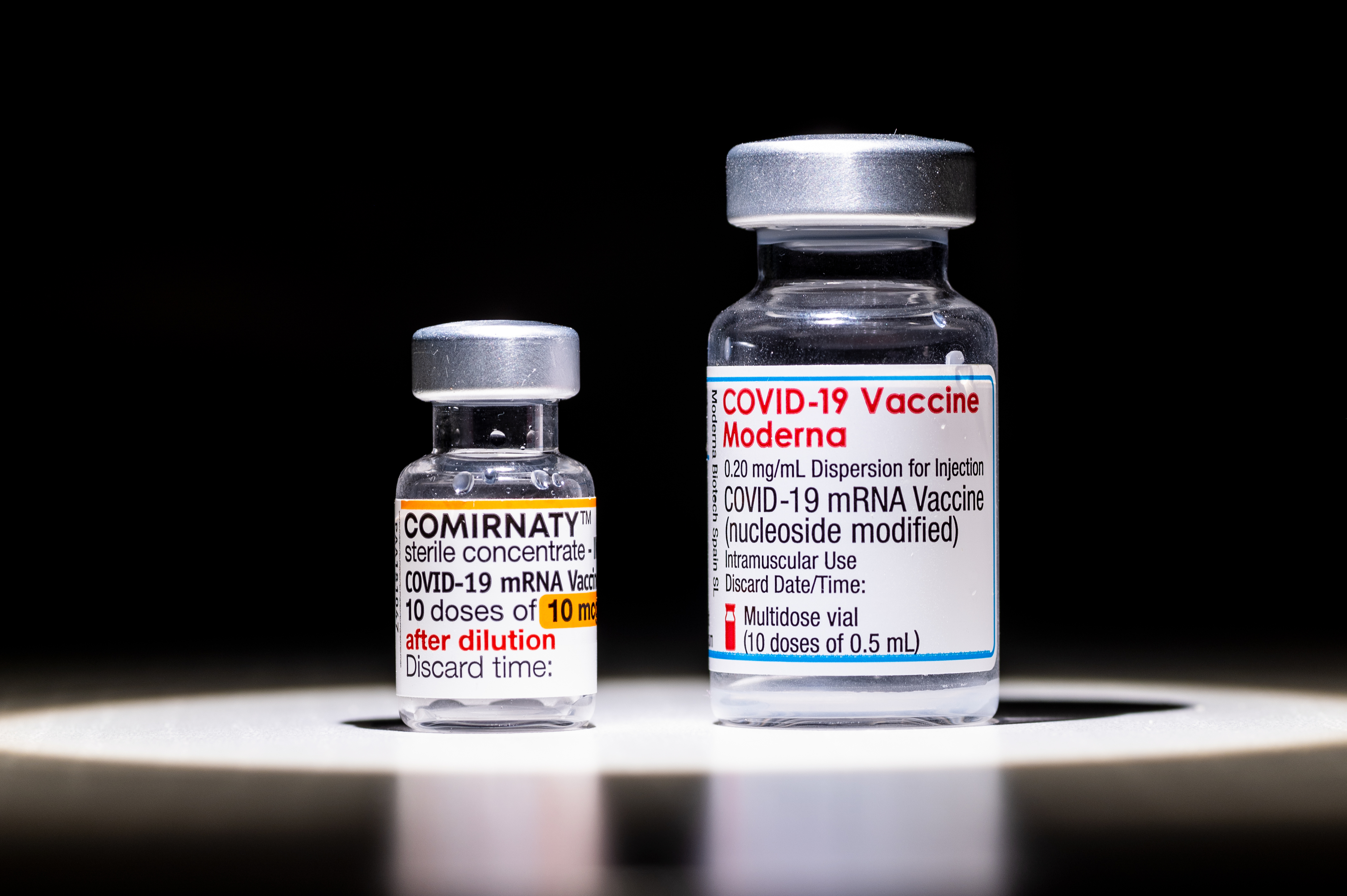 Two COVID-19 vaccine vials labeled Pfizer-BioNTech and Moderna on a surface