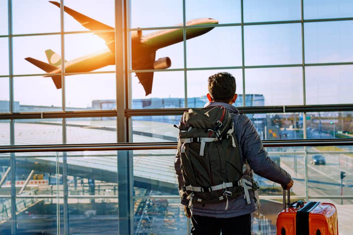 Person with backpack watching airplane take off from airport terminal window