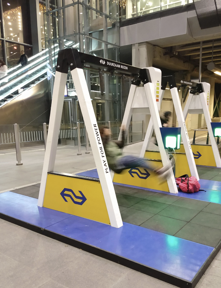 Swing set inside a train station with blurred motion of people swinging