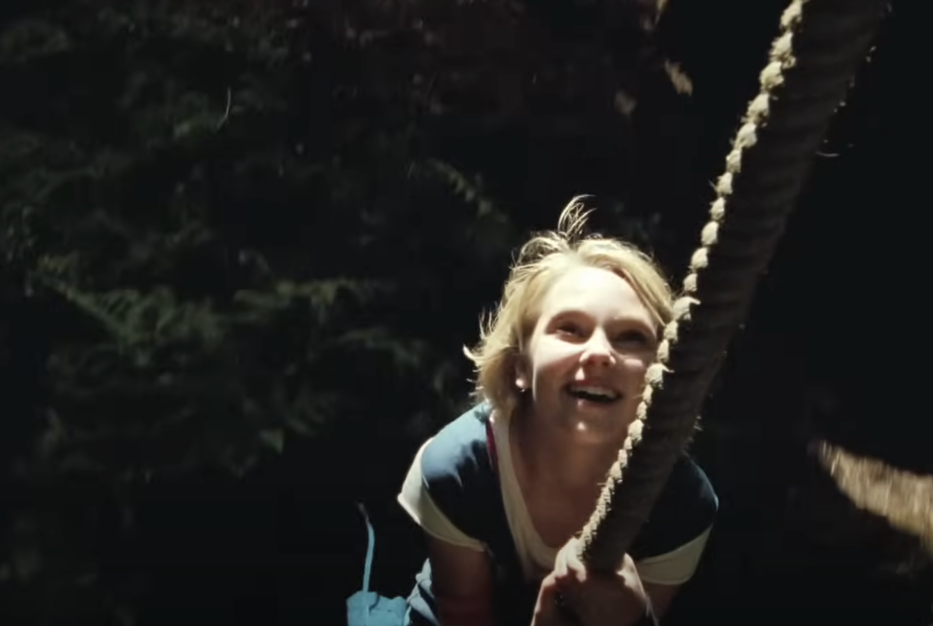 Person smiling and looking up while pulling on a thick rope, surrounded by darkness