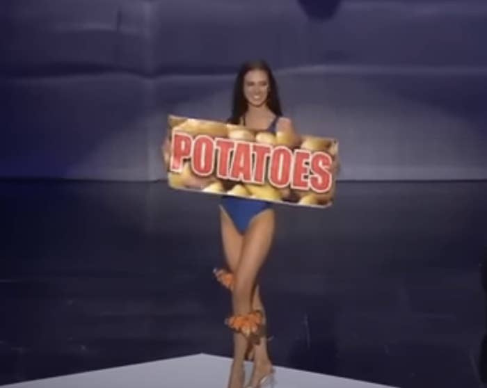 Woman in a dress holding a large sign with the word &quot;POTATOES&quot; on it