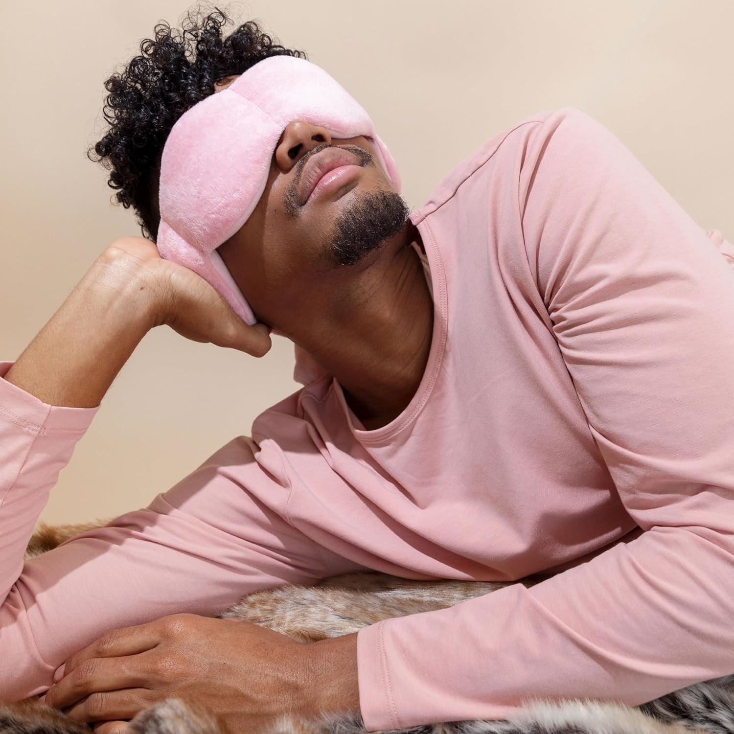 Person wearing a pink sleep mask and shirt resting head on hand, lying on a textured surface