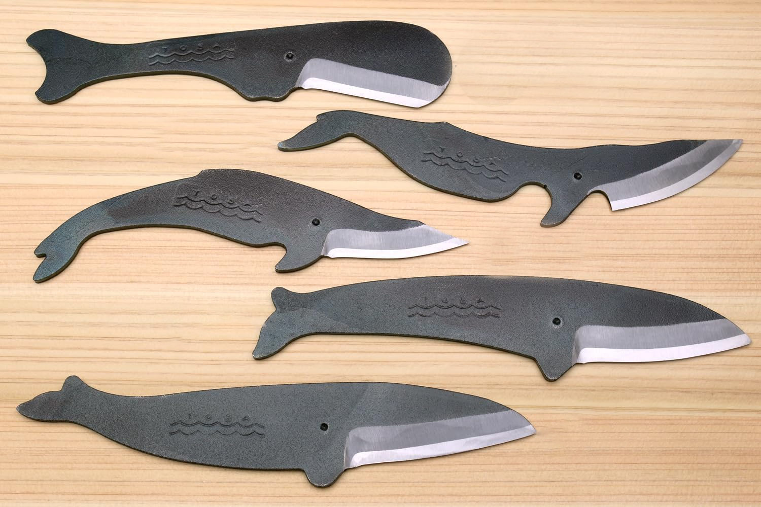 Six whale-shaped knives with unique blade shapes displayed on wooden surface