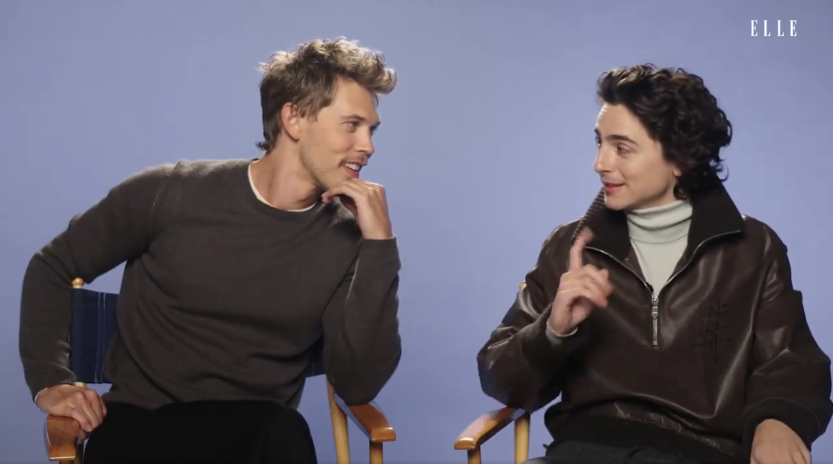 Timothée Chalamet and Austin Butler sitting, one in a sweater and jeans, the other in a leather jacket and turtleneck, engaging in conversation