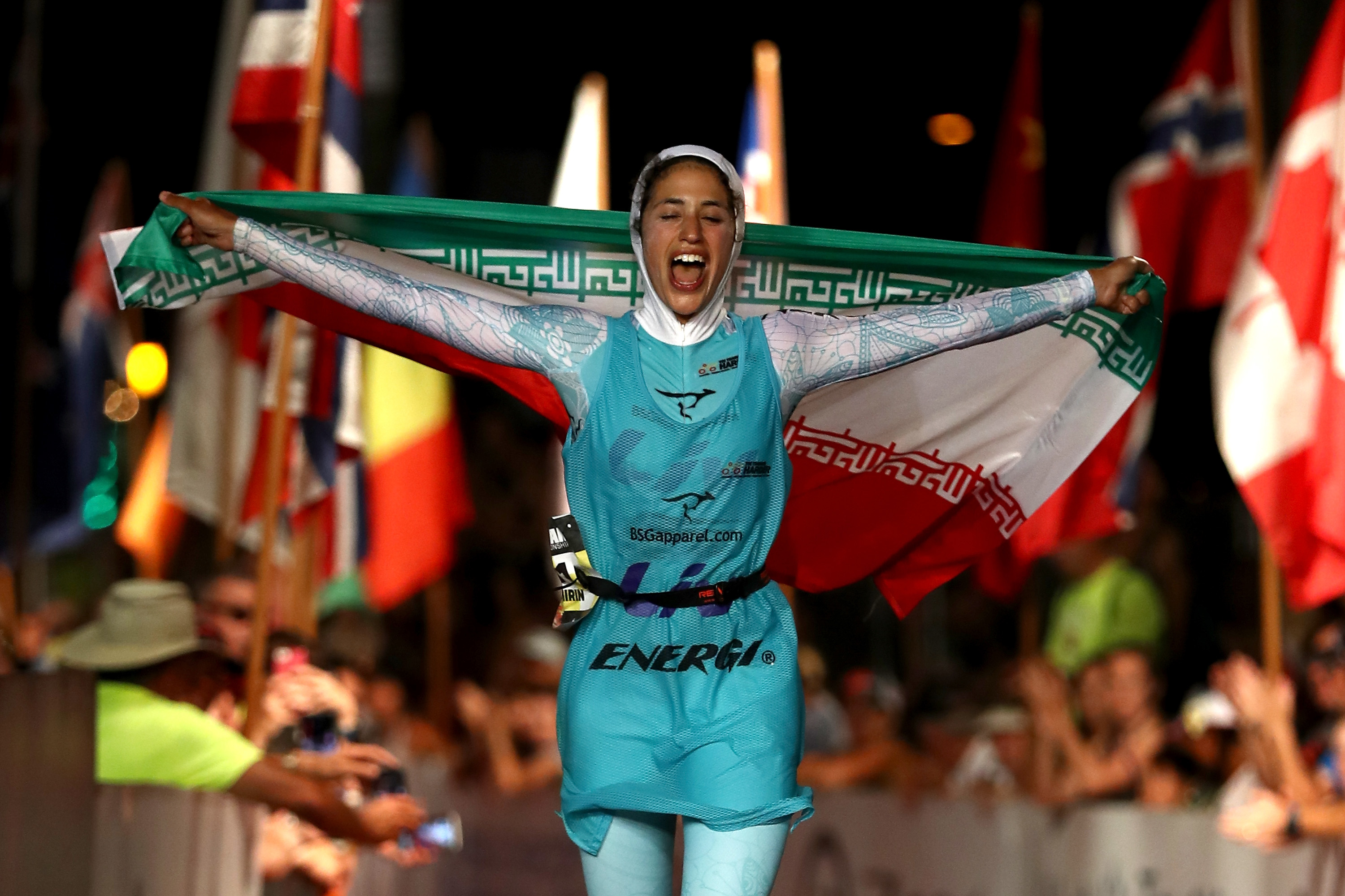 Shirin Gerami holding Iranian flag high with other flags in background; expressing triumph