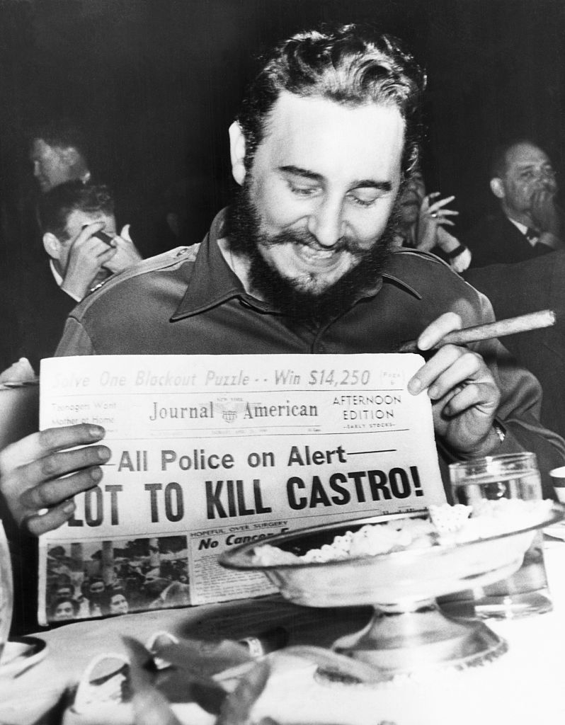 Castro smiling and holding a newspaper with headline &quot;Plot to Kill Castro&quot;