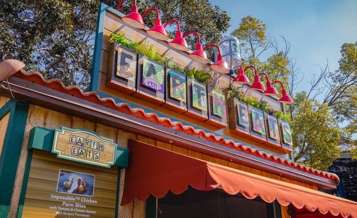 Food booth with sign &quot;Earth Eats&quot; and plant decor, serving Impossible Chicken and Citrus
