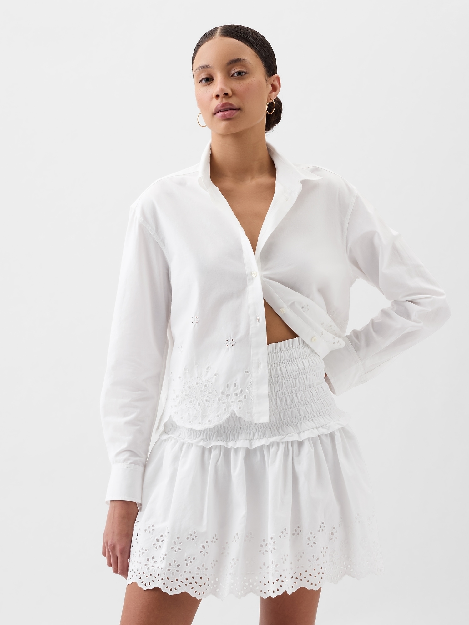 Woman in a white blouse and skirt with eyelet detailing, hand on hip, posing for a shopping article