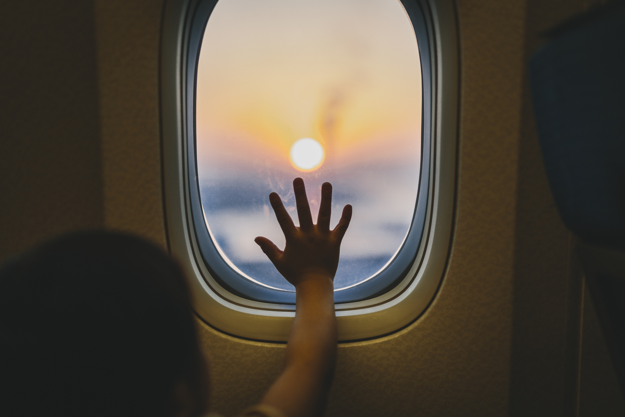 子供の手が飛行機の窓に触れている、外は夕焼け。
