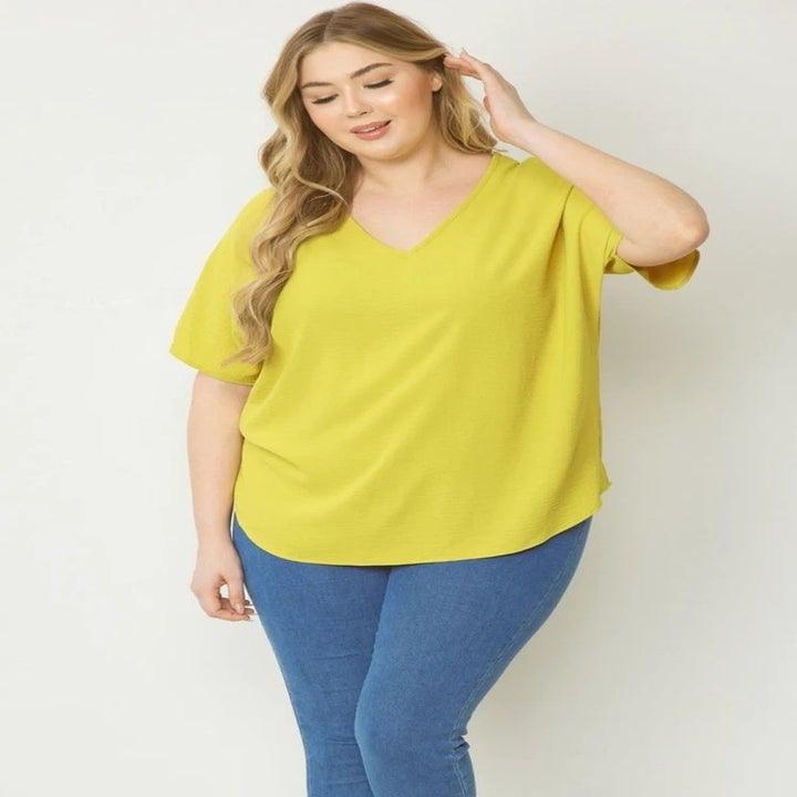 Woman in a casual, yellow v-neck top and blue jeans posing for the camera