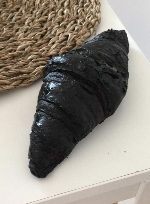 A black croissant on a white surface near a woven basket