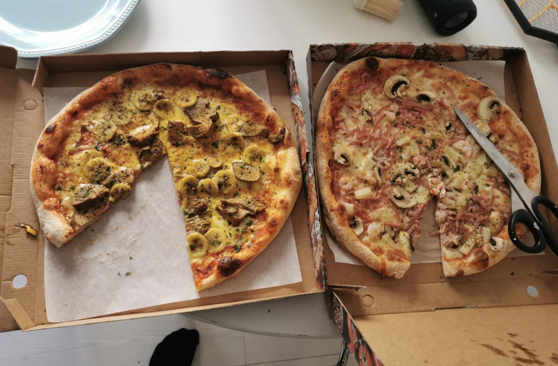 Two pizzas in open boxes, one half-eaten with a slice removed, and a pizza cutter rests on the other