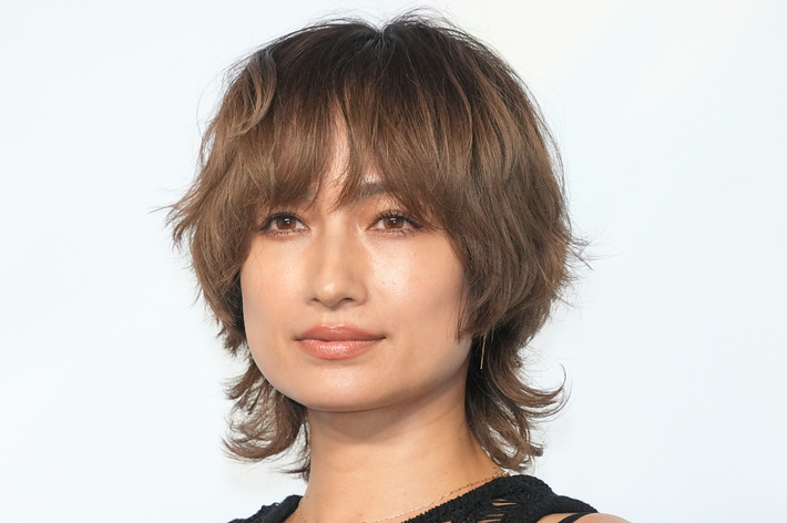 著名人がカメラを見つめ、手に化粧品を持っている。