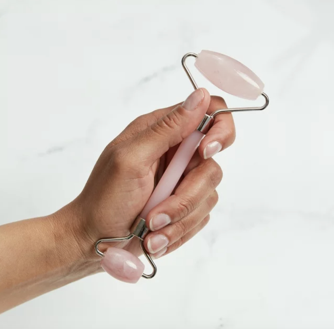 Hand holding a rose quartz facial roller against a white background