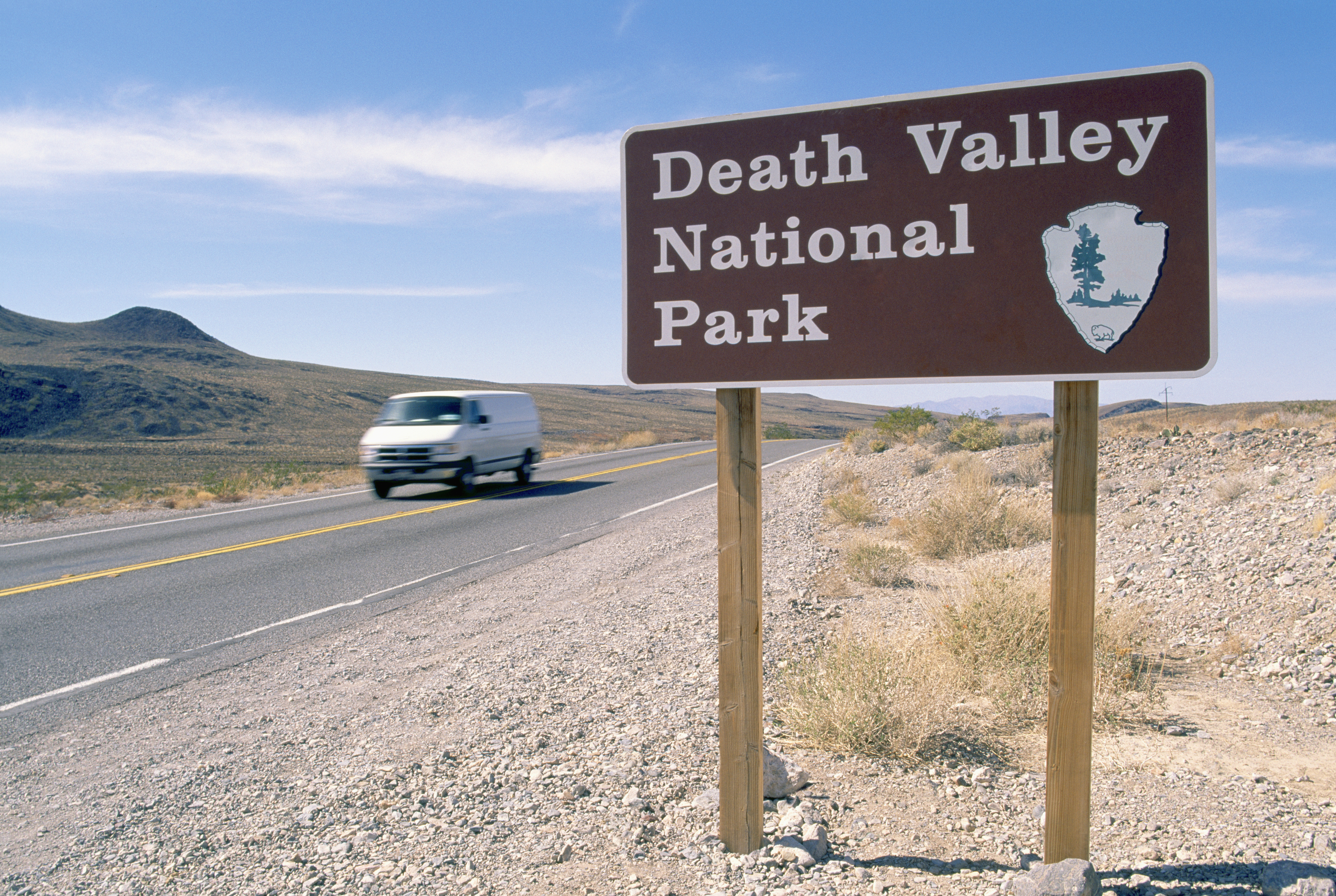 Sign for Death Valley National Park beside a road with a passing vehicle