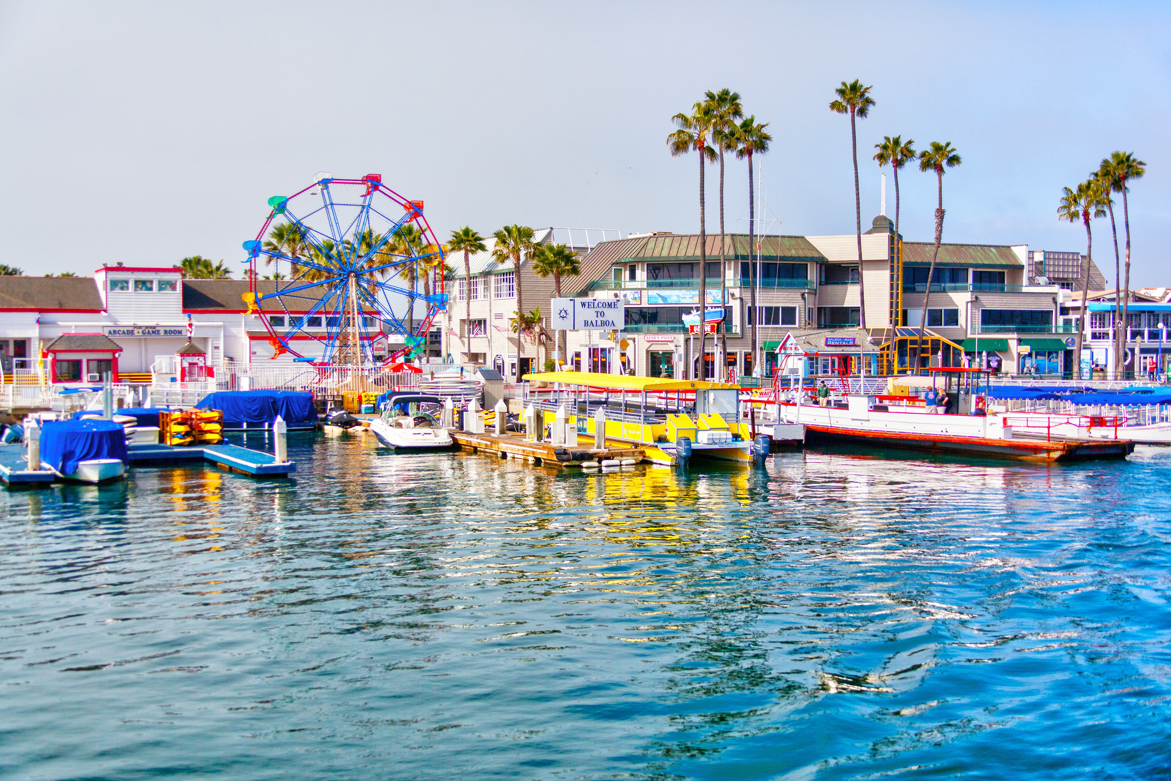 View of a waterfront with boats, a Ferris wheel, and palm trees, depicting a leisure travel destination