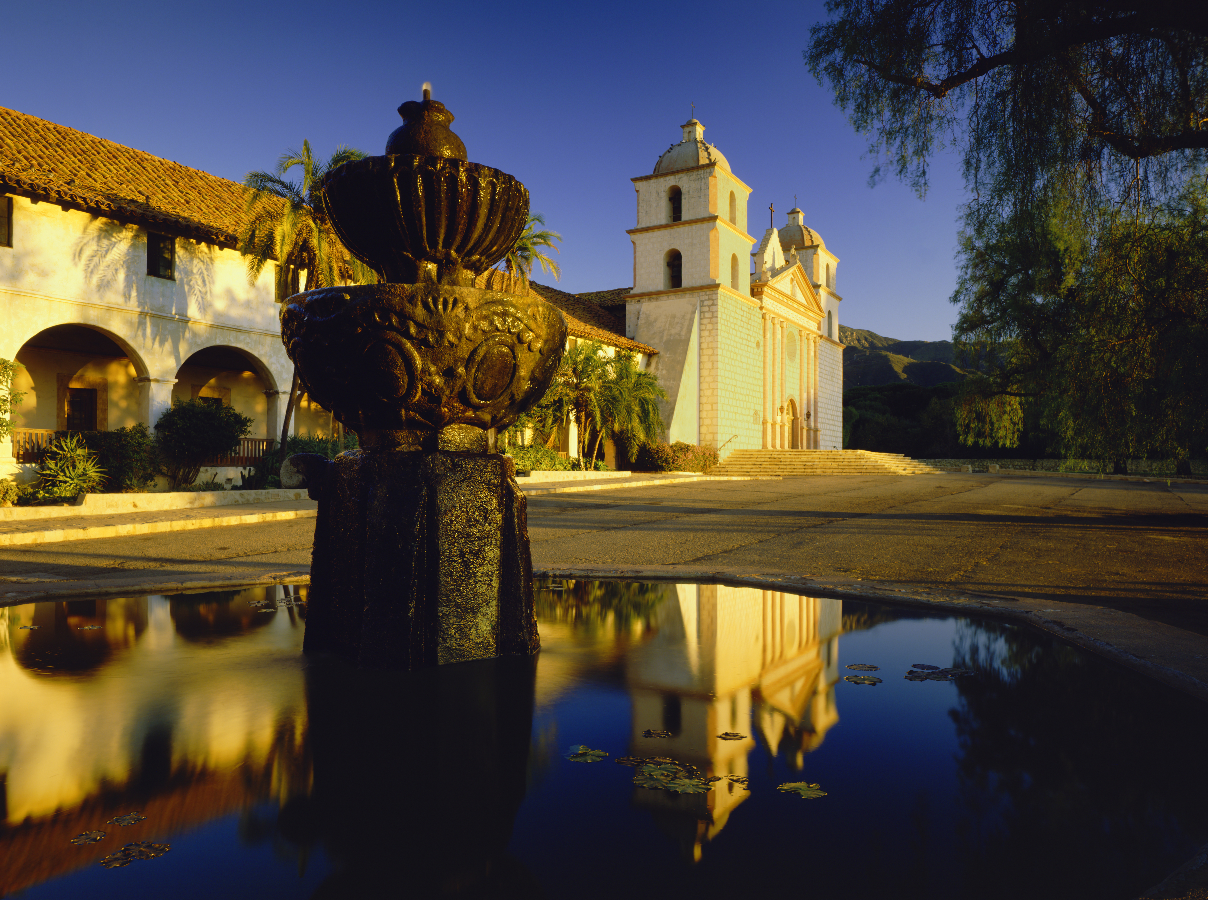 Historical mission building with a fountain in the foreground, reflecting on water