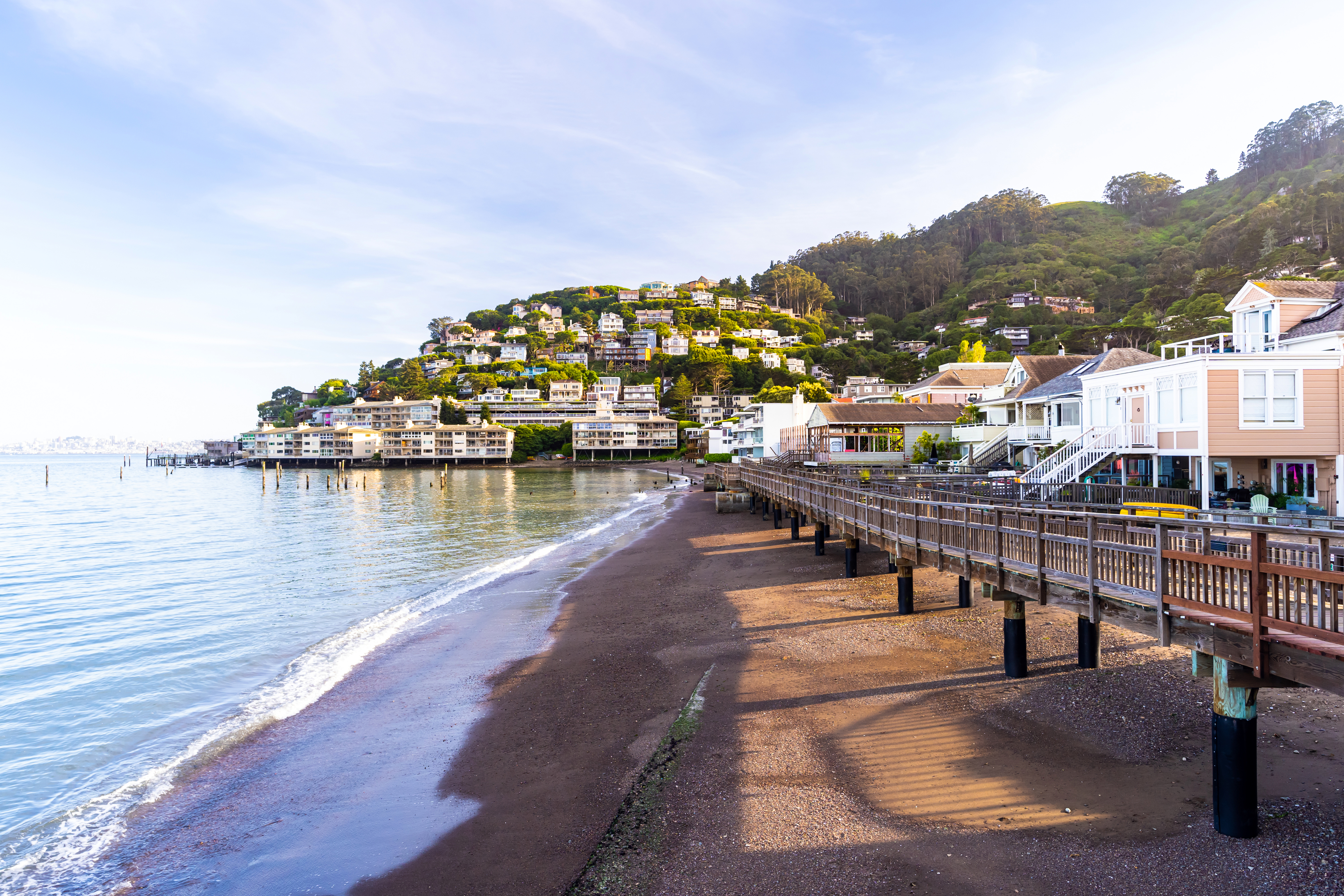 Scenic view of a coastal town with a pier, houses on a hillside, and calm waters