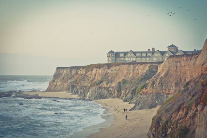 Cliffside coastal hotel with a walking couple on the beach below