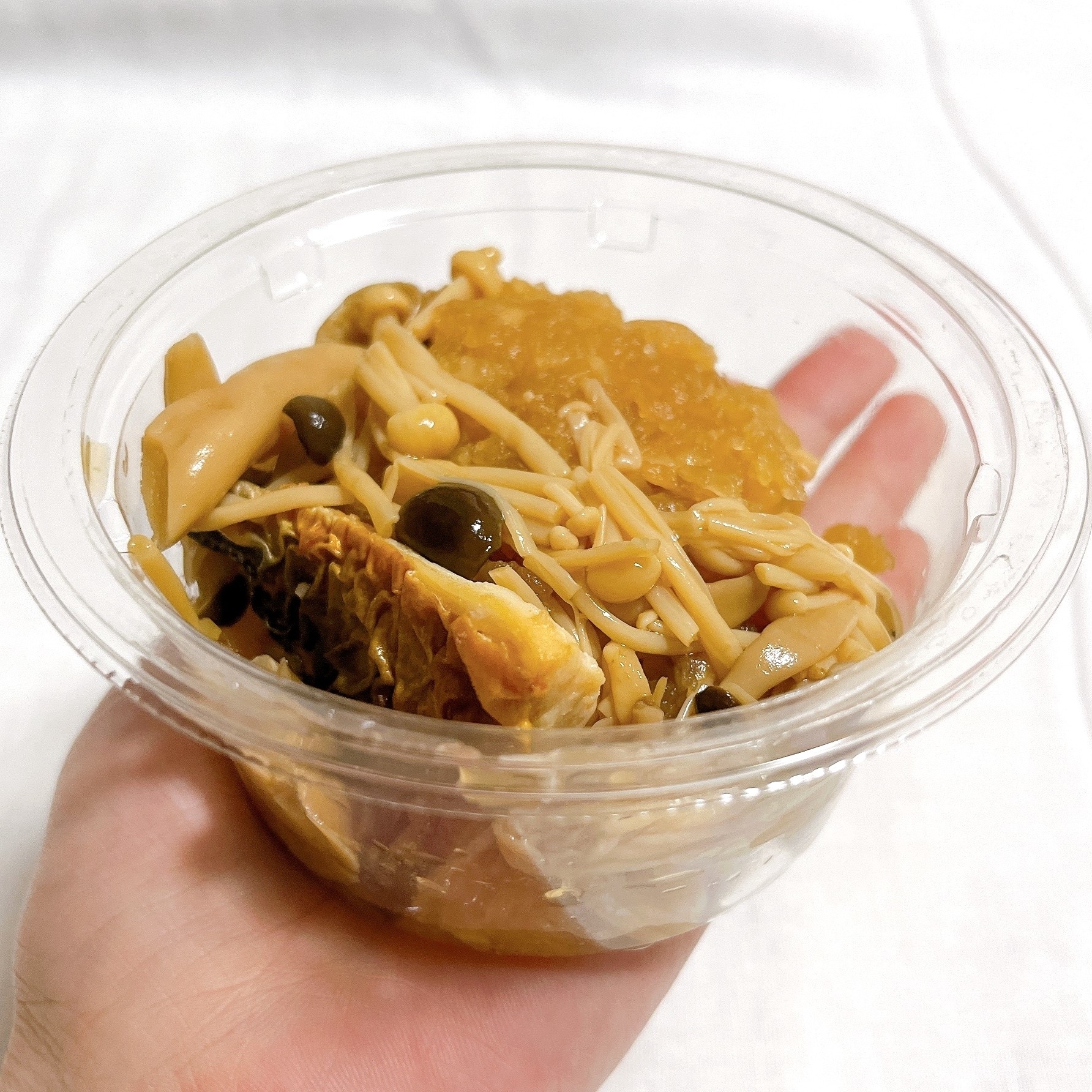 手に持たれた透明な容器に入ったキノコとワラビの和え物。