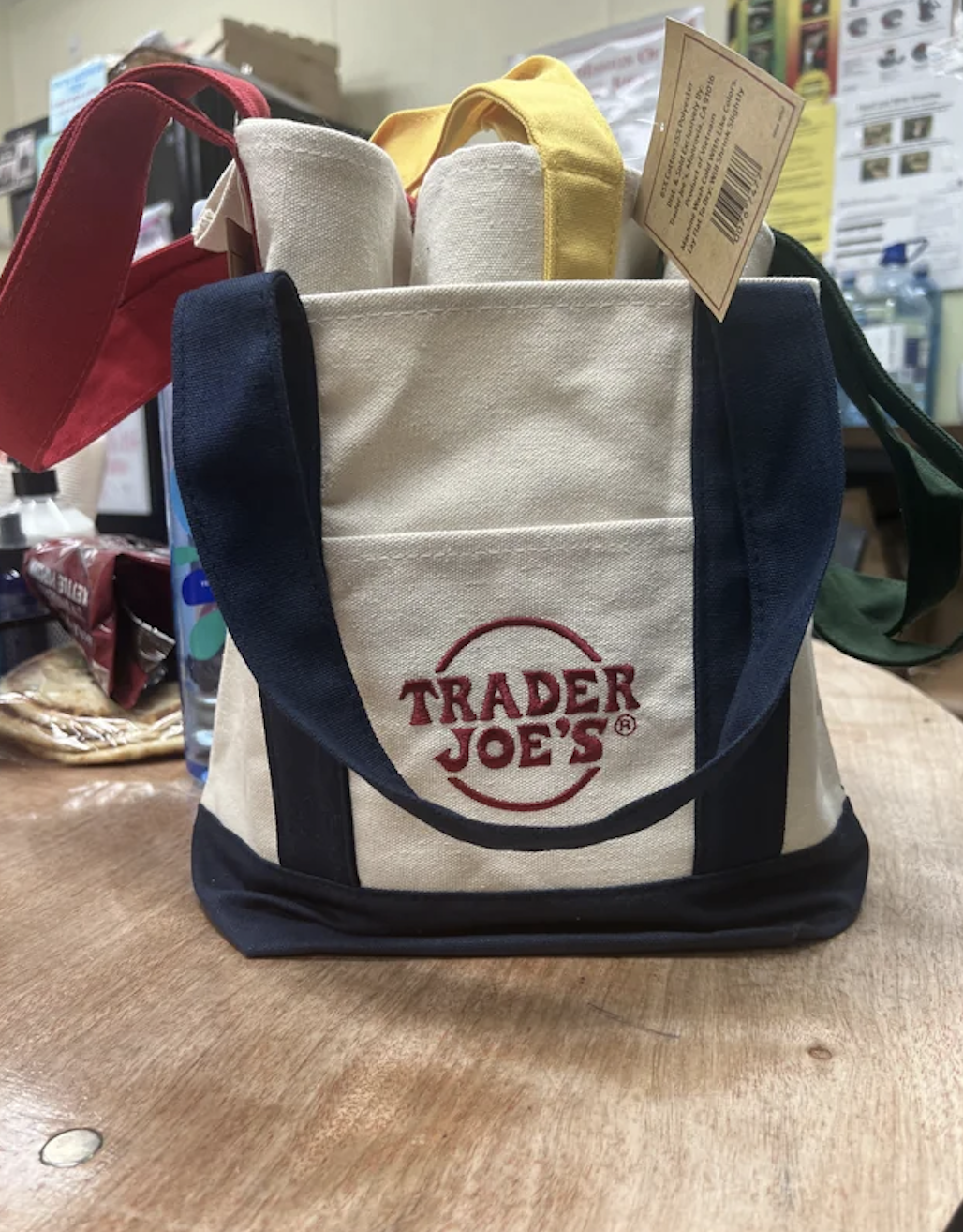 Trader Joe&#x27;s branded canvas grocery bags with various colored handles displayed on a counter