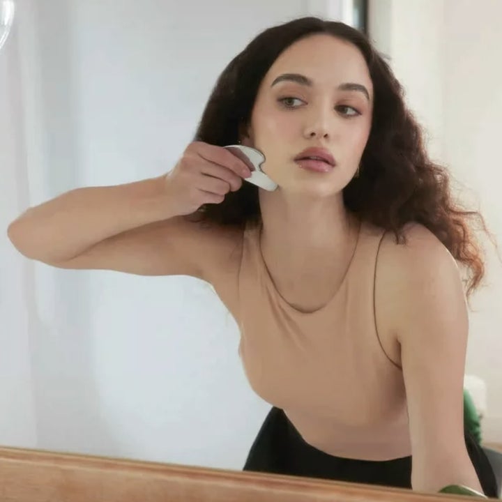 Person using a gua sha tool while looking at mirror