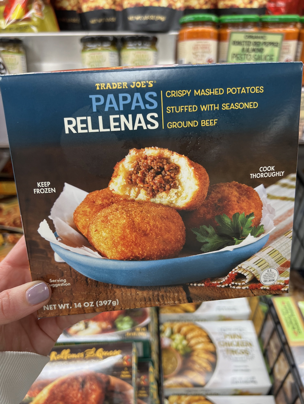 Hand holding a Trader Joe&#x27;s box of Papas Rellenas with a visible cooked product on the cover