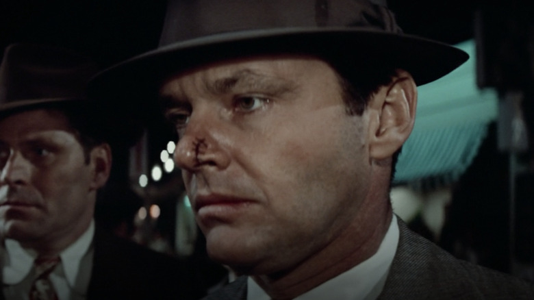 Man in fedora, close-up on tense expression, another man in a hat behind him