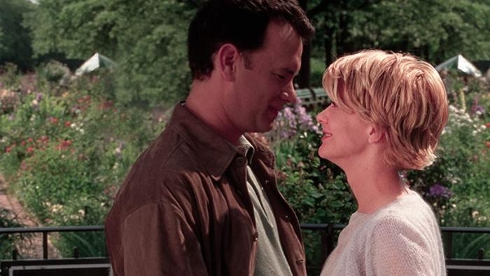 Tom Hanks and Meg Ryan standing close, facing each other with a backdrop of flowers