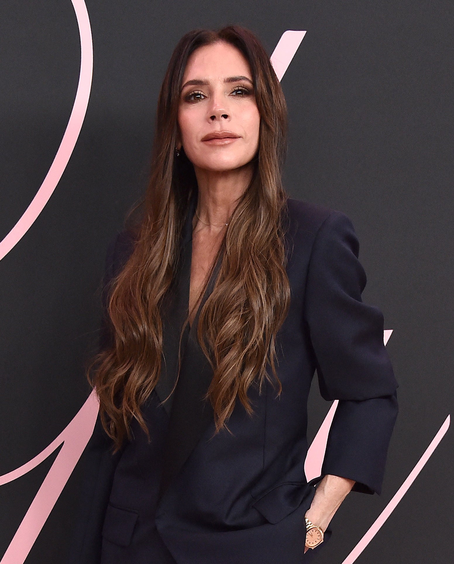 Victoria Beckham in a tailored pantsuit with pockets, standing confidently on a pink carpet