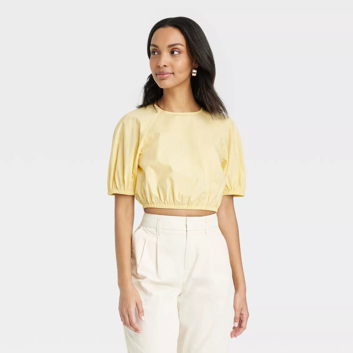 Model in a yellow cropped blouse and high-waisted white pants, standing posed for a fashion showcase