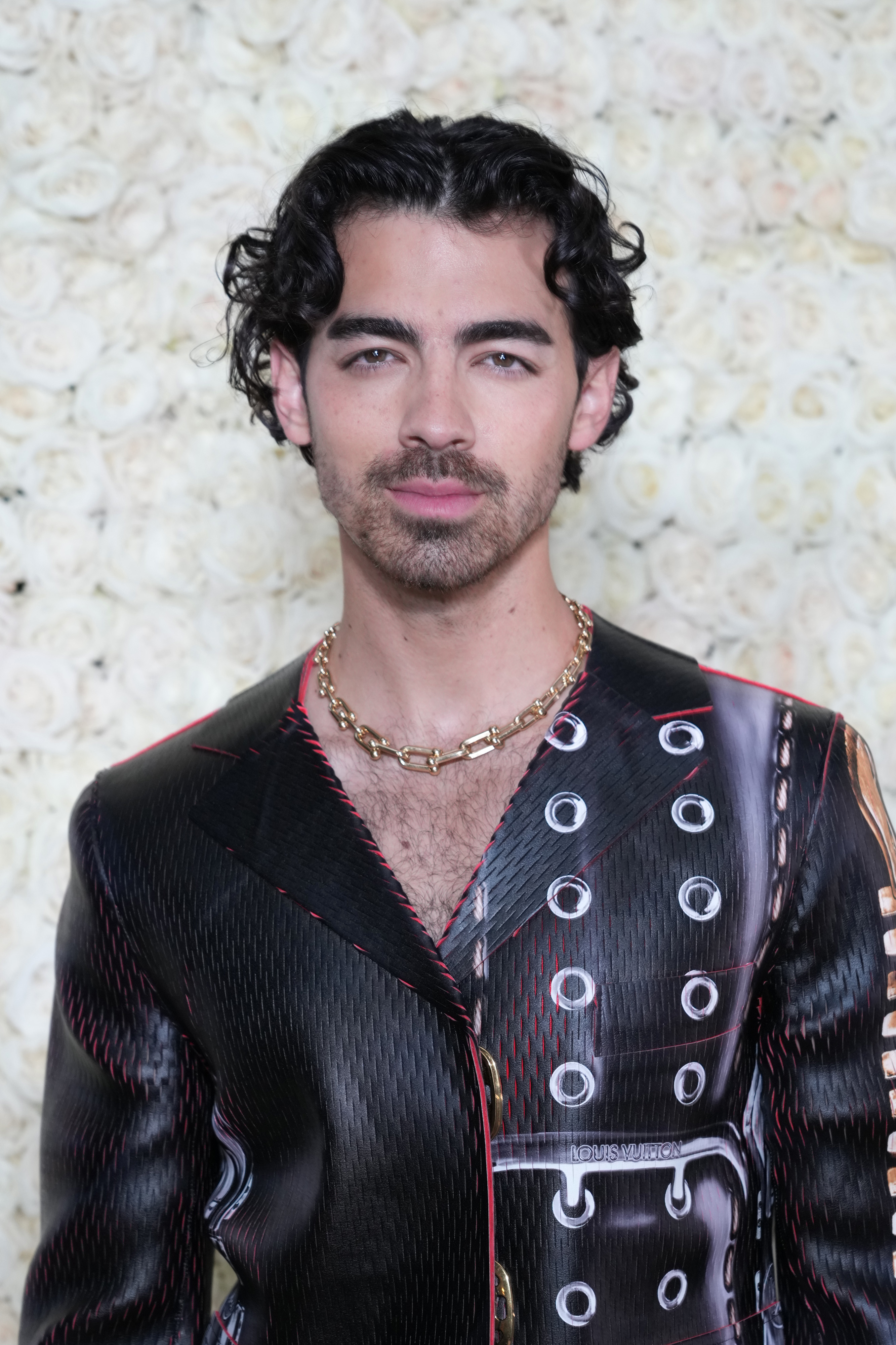 Joe Jonas wearing a patterned suit jacket with metal details and a necklace