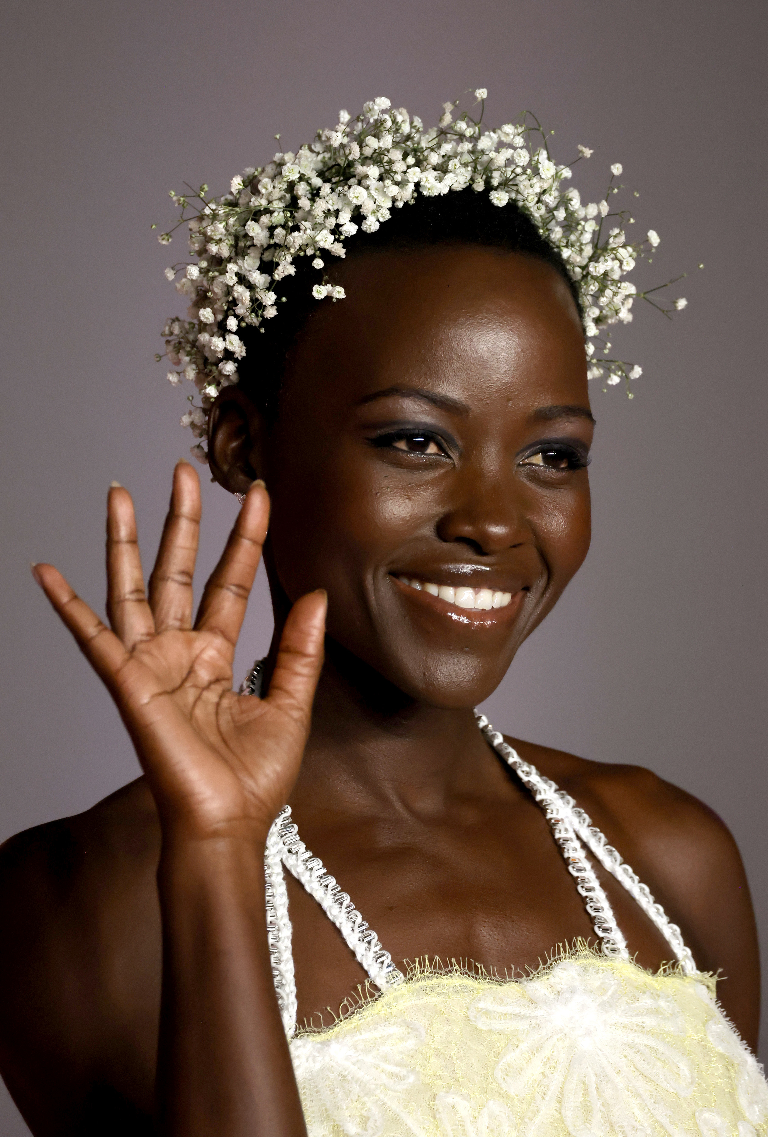 Lupita Nyong&#x27;o smiles, waves in a floral headdress and embellished dress