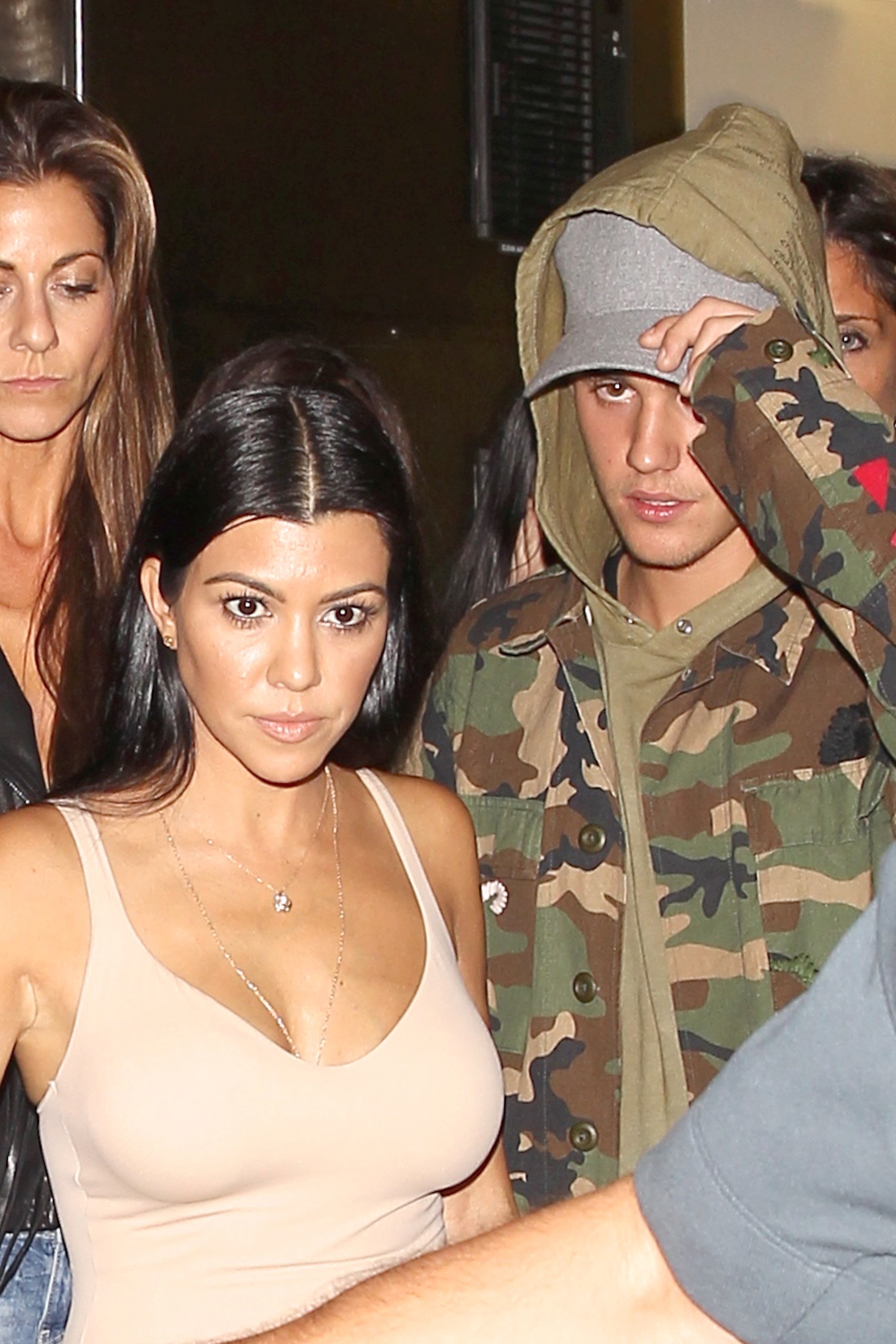 Kourtney and Justin walk together; her in a tank top and him in a camouflage hoodie and cap. They appear to be avoiding the camera