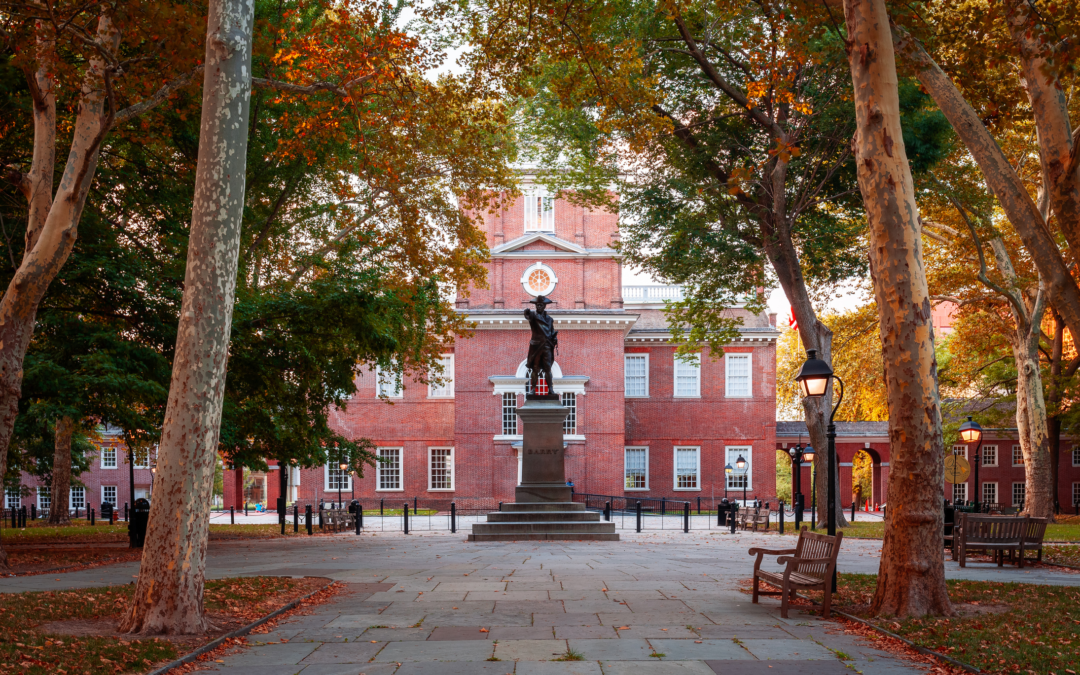 Historic brick building with a central clock and statue in a treelined courtyard