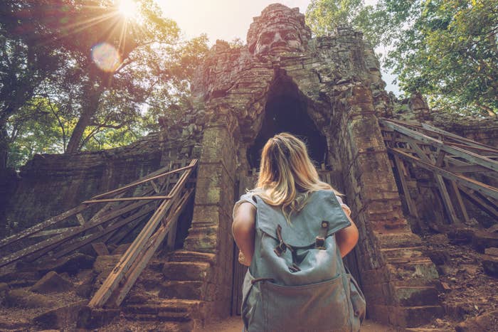 Woman with backpack facing an ancient temple entrance surrounded by trees