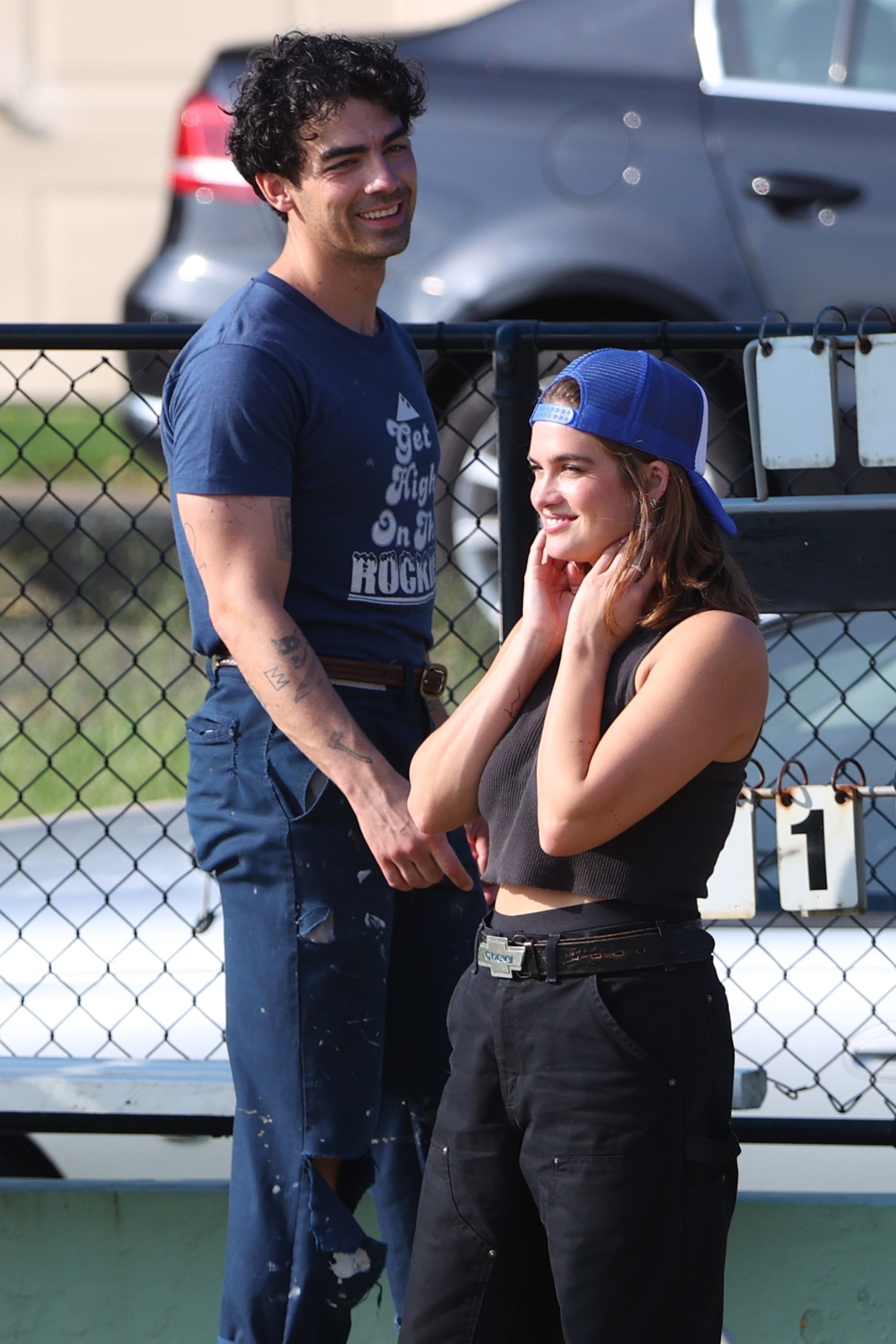 Joe in a casual t-shirt and Stormi in a crop top and high-waisted pants smiling as they hang outside