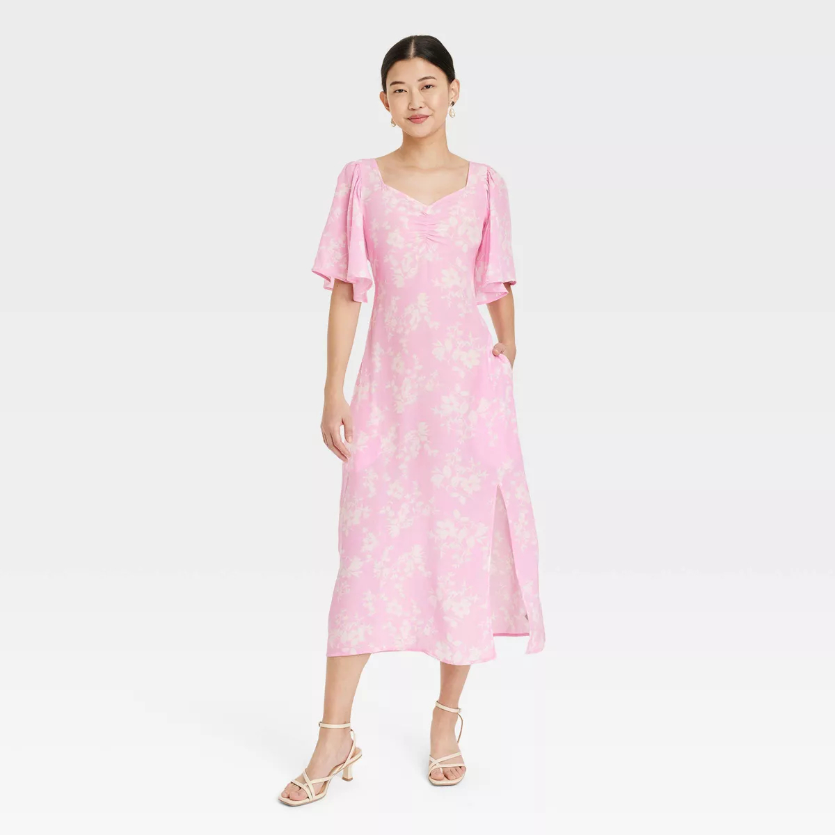 Model wearing a pink floral midi dress with puff sleeves and v-neckline, paired with strappy sandals