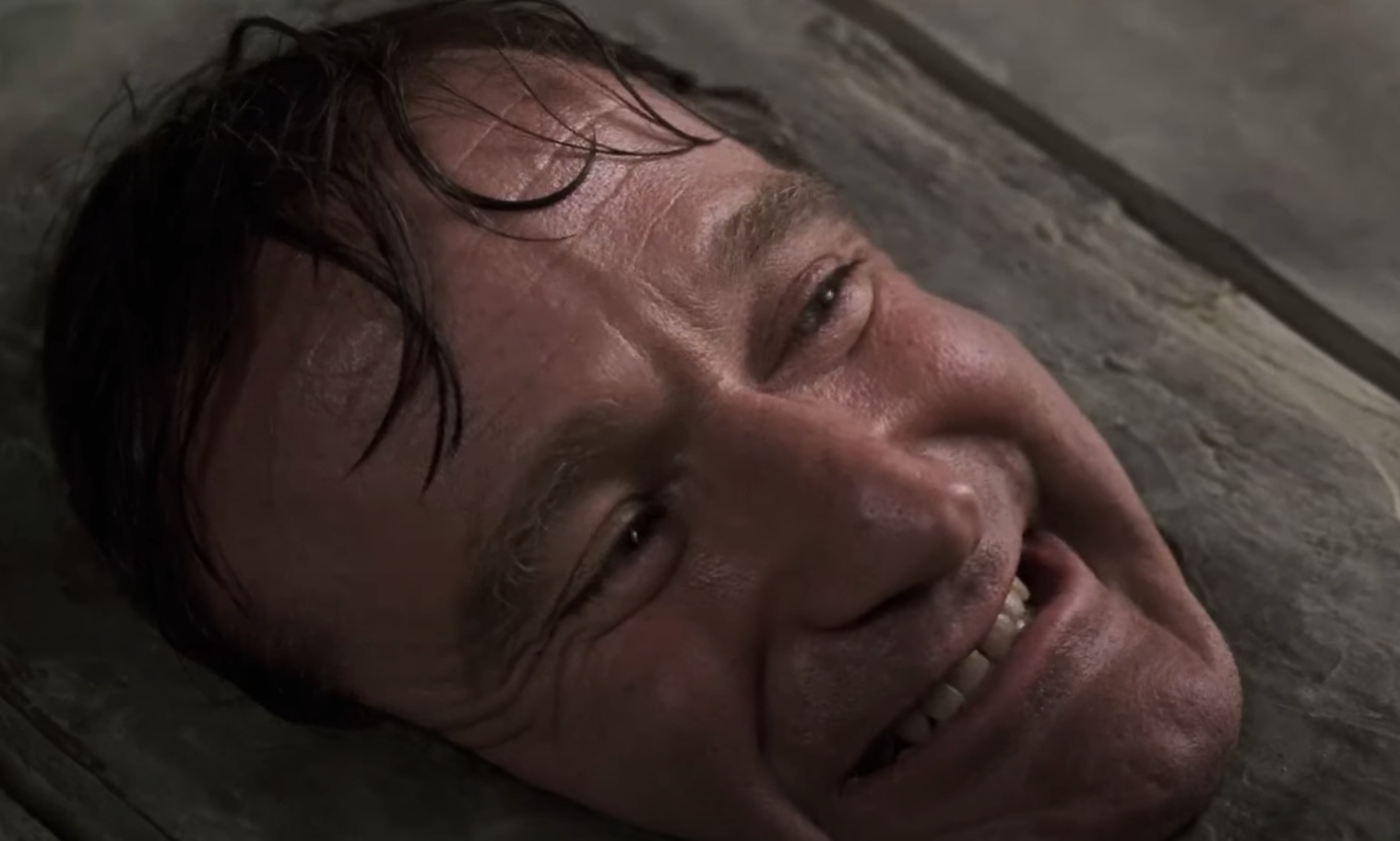 Close-up of a male character from a film, smiling while lying on his back, in an indoor setting