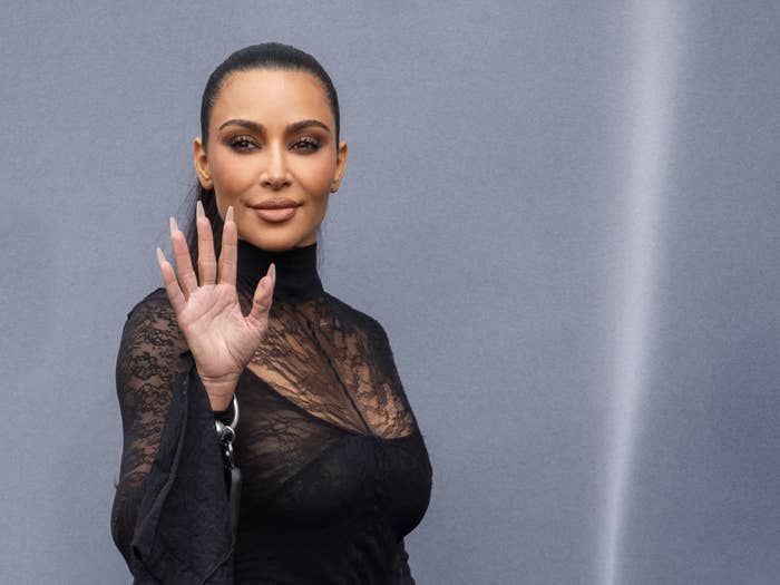 Kim Kardashian wearing a lace-detail outfit, waving to the camera