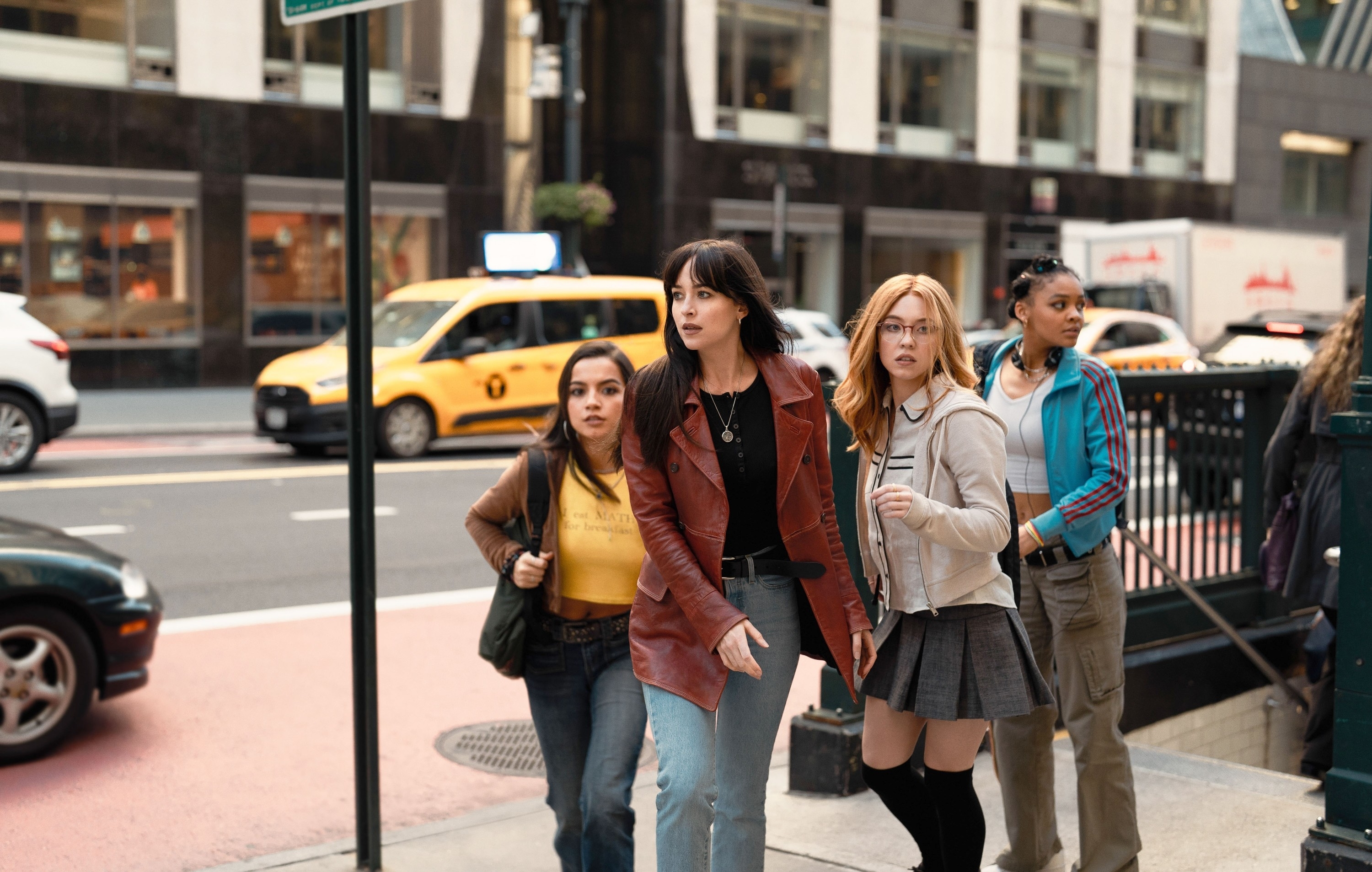 Four women walking on a city street, appearing engaged in conversation, dressed in casual attire in a scene from Madame Web