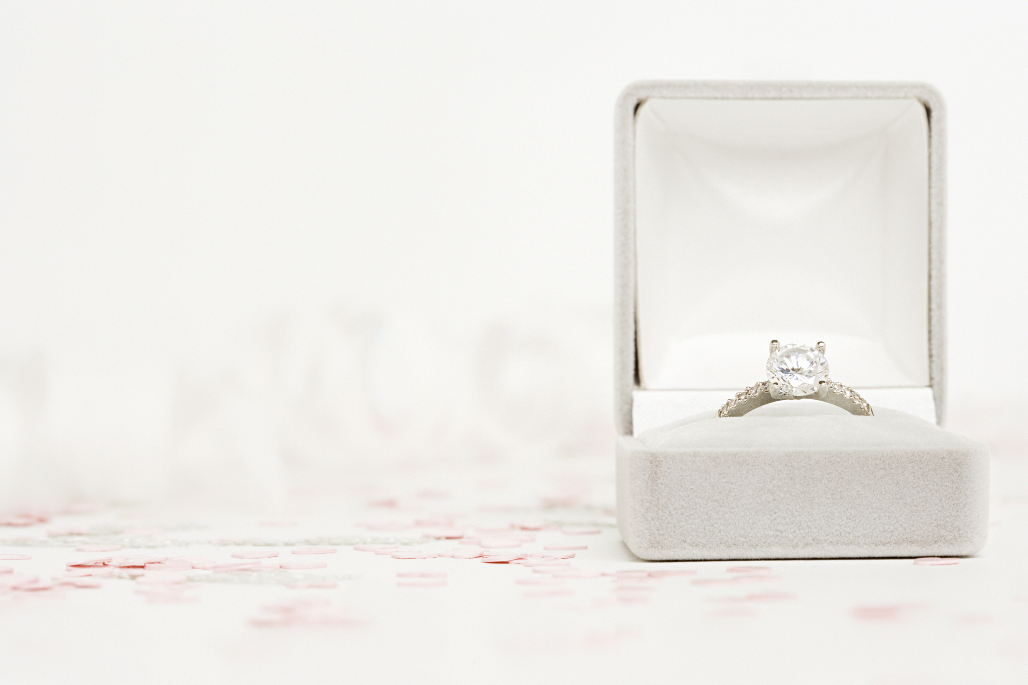 Engagement ring in an open box with tiny heart confetti scattered around