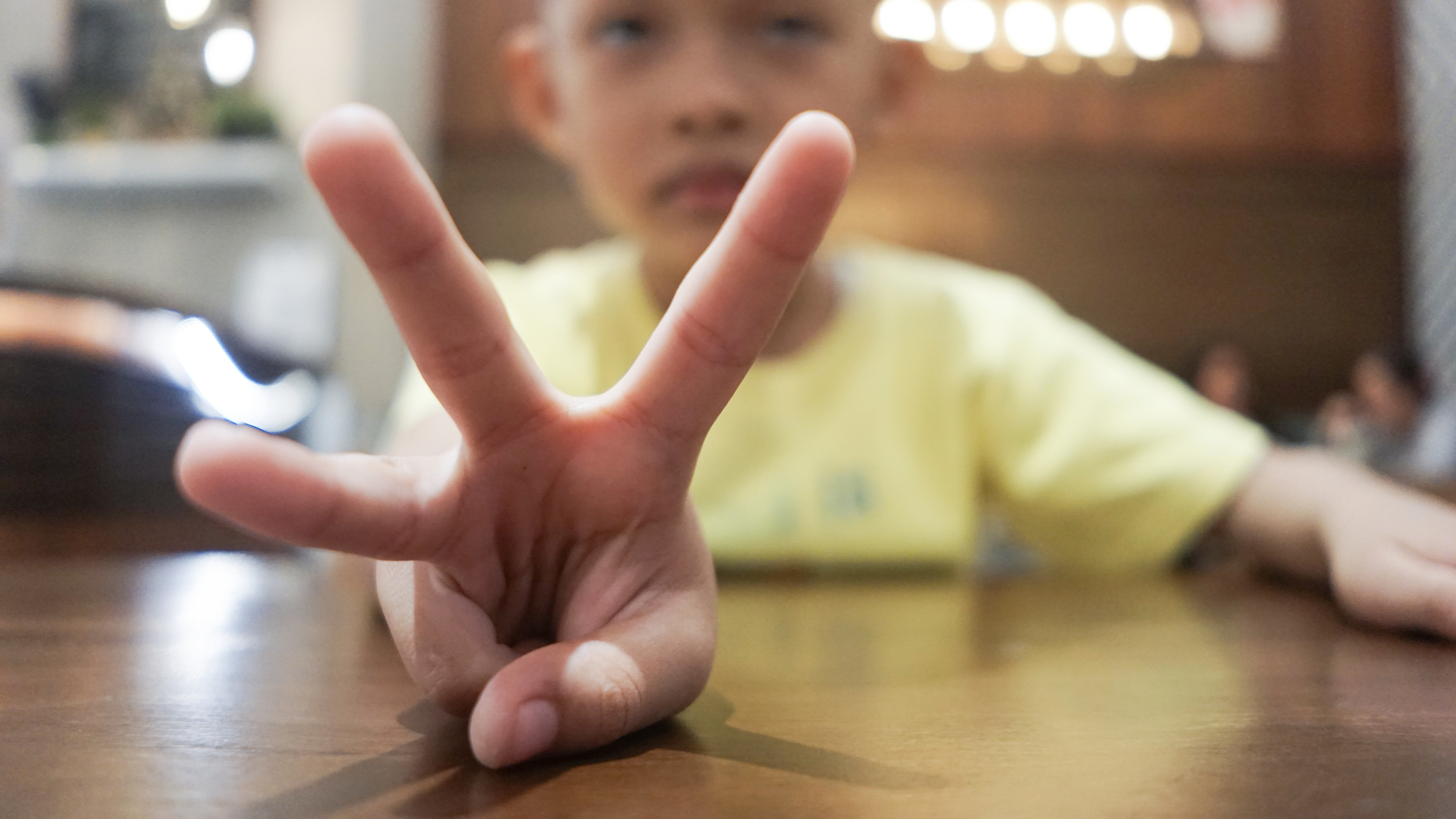 Child making a peace sign with hand, blurred background, emphasis on communication and connection