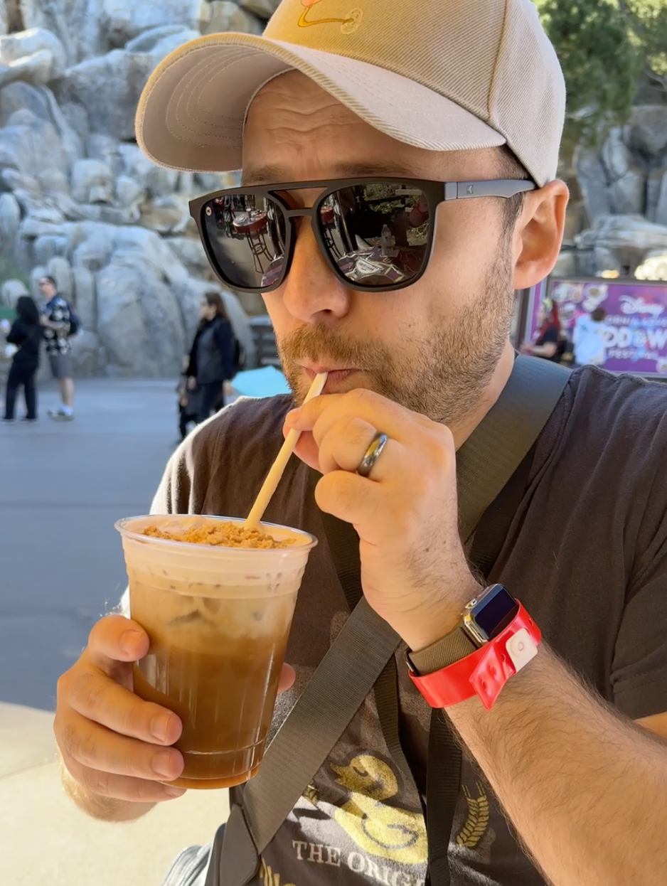 Man sipping a drink with a straw, wearing a cap and sunglasses, at an outdoor venue