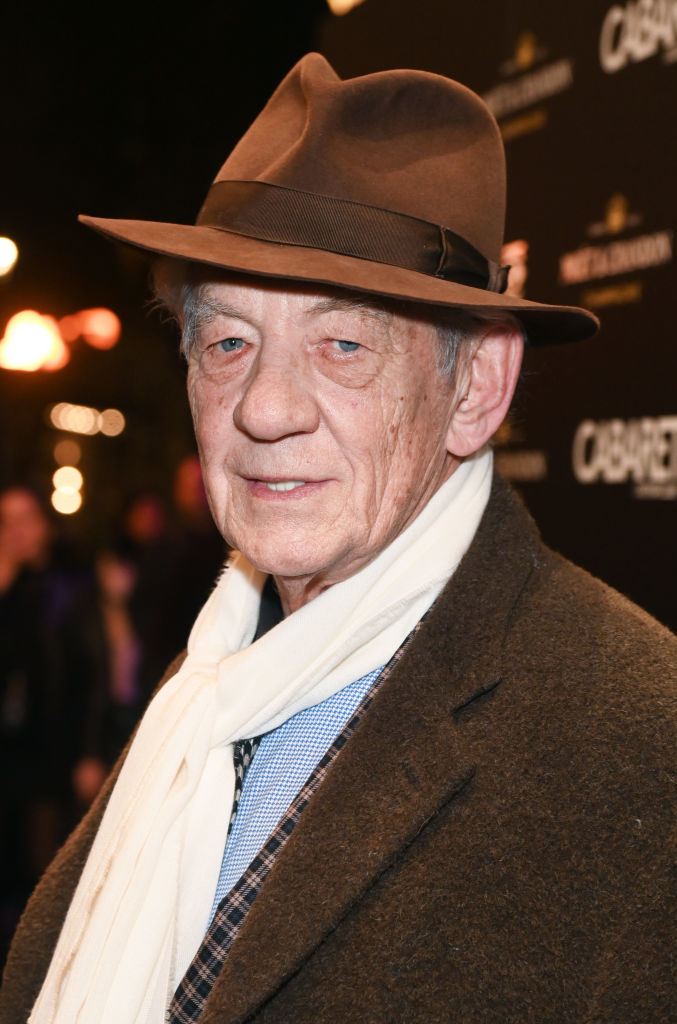 closeup of Ian in a fedora hat and scarf over a blazer, looking at the camera
