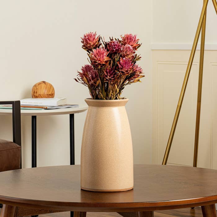 Vase with dried pink flowers on a wood table, gold floor lamp and chair in the background
