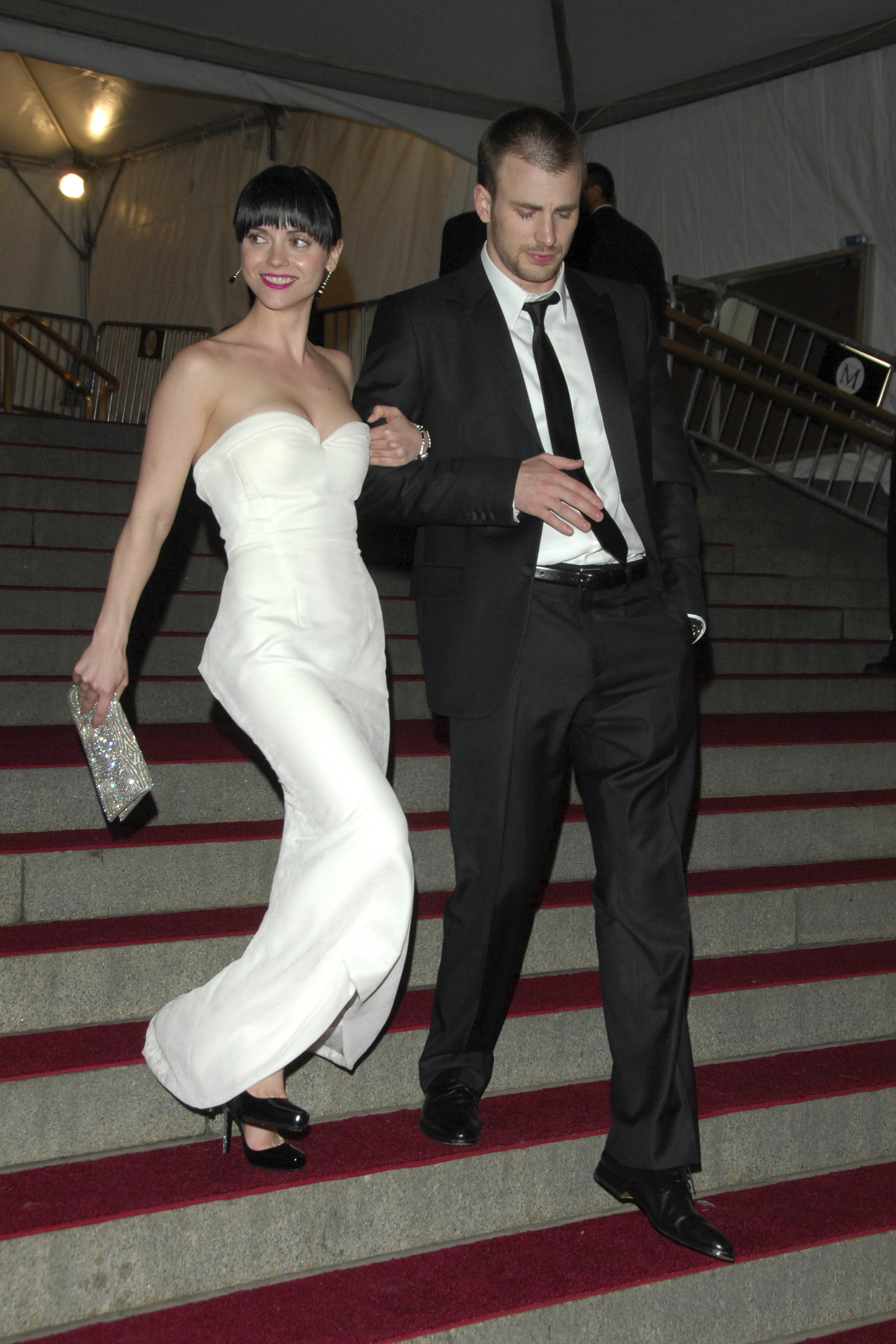Christina smiling in a strapless white gown and Chris in a black suit and tie, walking on a staircase