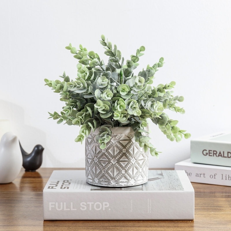 Artificial green plant in a white textured pot, displayed on a stack of books on a wooden table