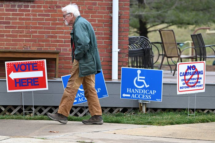 A person walks past signs indicating a voting site with handicap access and campaigning restrictions